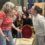 Two women engaged in a heated conversation with a group of onlookers showing varied reactions in the background.