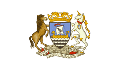 A coat of arms featuring a horse and a unicorn standing beside a shield with a ship and waves. An ornate crown tops the shield, and a ribbon at the bottom reads “MED LOGUM SKAL LAND BYGGES.”.