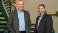 Two men in business suits standing next to stairs.