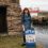 A woman standing next to a sign that says open.