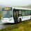 A white bus with "LERWICK E" displayed on the front LED screen is driving on a wet countryside road, with misty hills and scattered houses in the background.