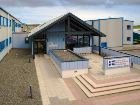 Exterior view of the University of the Highlands and Islands Shetland College entrance with surrounding buildings and signage.