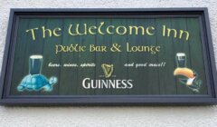 Sign for "The Welcome Inn" highlighting beer, wine, spirits, and "good craic," with Guinness branding, featuring illustrations of a turtle with beer and a toucan with beer.