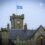 A stone building with a clock tower, featuring a blue and white flag at the top. Text in the image reads "Lerwick Town Hall.