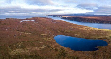 Aerial view of a vast, brown-colored landscape with a large blue lake and a smaller waterbody, bordered by hills and a distant coastline under a partly cloudy sky.