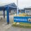 Entrance sign for Sandwick Junior High School, featuring a blue and yellow color scheme. The school building is visible in the background.