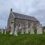 A small stone church with several old, weathered gravestones in front, set against a cloudy sky.