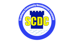 Logo of the Scalloway Community Development Company, featuring the initials SCDC in yellow on a blue castle motif, encircled by the organization’s name and an illustration of water waves.