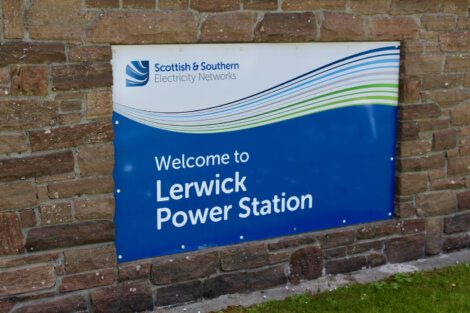 Sign reading "Welcome to Lerwick Power Station" with the logo of Scottish & Southern Electricity Networks against a brick wall background.