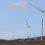 Wind turbines placed on a hilly landscape under a clear sky.