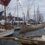 A row of boats with colorful flags docked at a marina during an event. Overcast sky in the background.