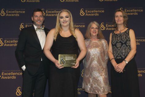 Four people stand in front of a Scotland Food & Drink Excellence Awards backdrop. One person holds a plaque that reads "Excellence Awards 2023". They are all dressed in formal attire and smiling.