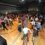 People dancing and socializing at an indoor event or gathering with tables set around the perimeter of the dance floor.