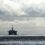 Offshore oil rigs and a supply vessel at sea under a cloudy sky.