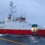 A red and white fishing boat named "antonio maria" at sea connected by a rope, with a dark sky above.