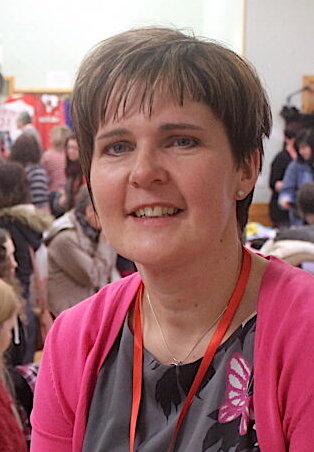 A woman with short hair smiling in a room with people in the background.