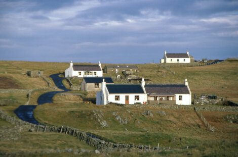 Rural landscape with winding road leading to white houses against a clear sky.