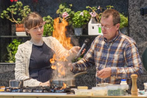 A man and woman standing in front of a stove with flames.