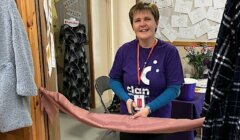 A woman cutting a ribbon in a room full of clothes.