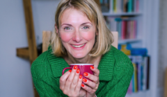 A woman holding a red mug in front of a bookcase.