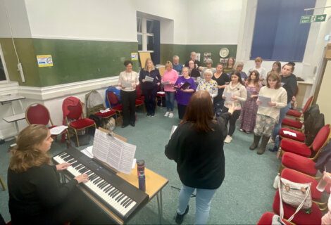 A group of people singing in a room with a piano.