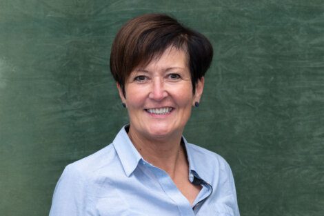 A woman in a blue shirt smiling in front of a green wall.