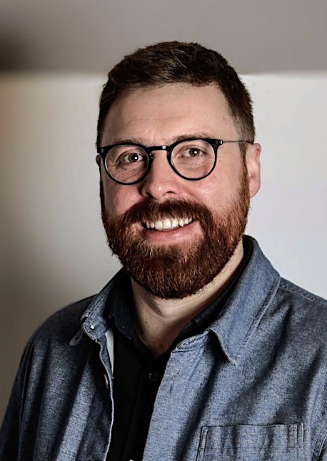 A man with glasses and a beard is smiling.