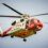 A red and white helicopter flying through the sky.