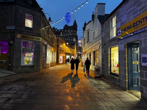 Two people walking down a narrow street at night.