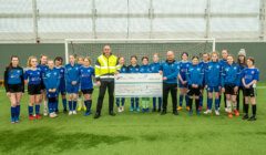 A group of soccer players posing with a cheque.