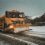 A snow plow driving down a snowy road.