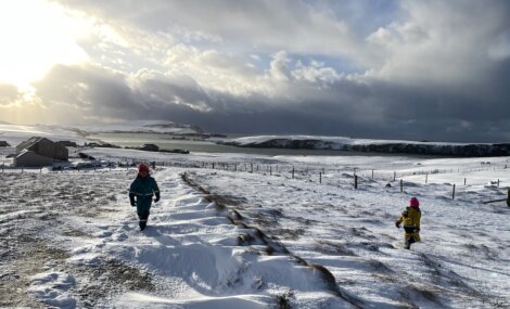 Two children walking down a snow covered hill.
