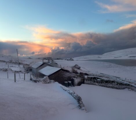 A snowy landscape with a house and a lake in the background.