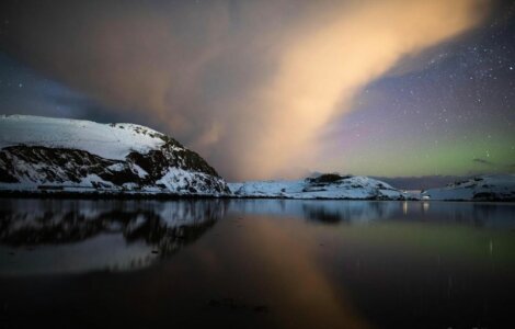 An aurora bore over a snow covered mountain.