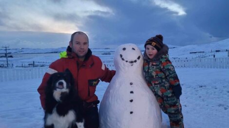 A man and a child standing next to a snowman.