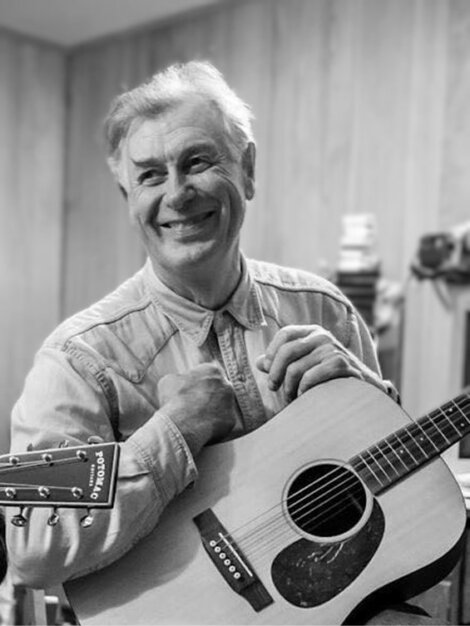 A man smiling while holding an acoustic guitar.