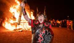 A man with a shield in front of a bonfire.