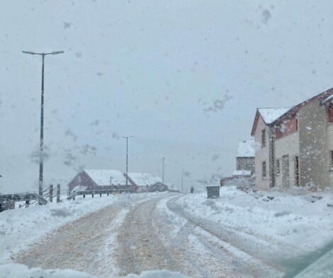 A snow covered road with houses in the background.