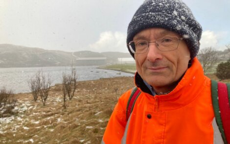 A man in an orange jacket standing next to a body of water.