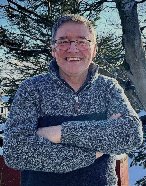 A man wearing glasses and a sweater in front of a tree.