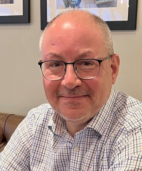 A bald man wearing glasses and a checkered shirt.
