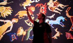A woman is standing in front of a projection of constellations.