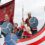 A family dressed as vikings with shields and a spear aboard a boat float with a dragon head design during a parade.