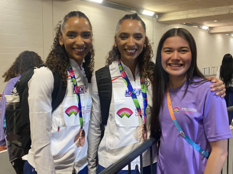 Three smiling individuals posing for a photo, two wearing matching uniforms with medals and one in a lavender shirt.
