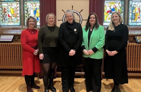 Five women standing in front of stained glass windows, posing for a group photo.