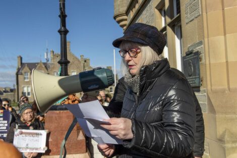 A person reading from a sheet of paper into a megaphone at an outdoor event.