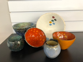 A collection of colorful ceramic bowls and a plate with decorative patterns displayed in front of a stack of white books.