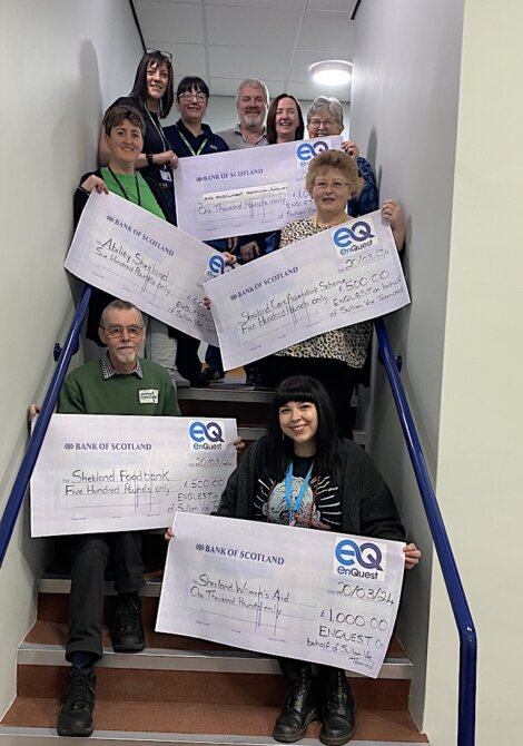 A group of people smiling on a staircase, holding large ceremonial checks for charity donations.