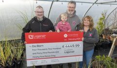 A group of people holding a check in front of a greenhouse.