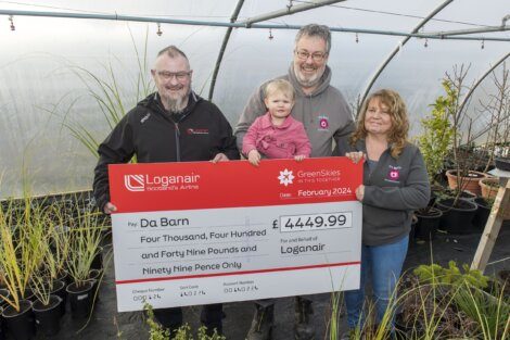 A group of people holding a check in front of a greenhouse.